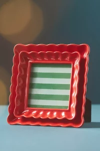 A red Scalloped Stoneware Picture Frame on a shelf. A cute and top rated Anthropologie home gift for displaying photos.